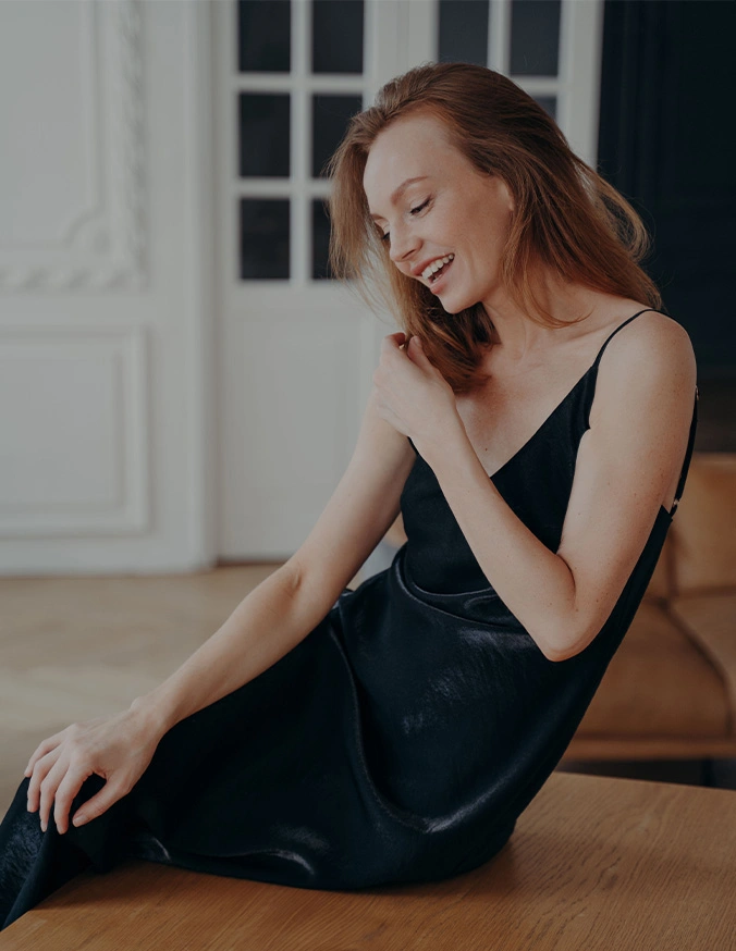 Woman in elegant black dress sitting on floor smiling, formal portrait in bright interior setting - Arm lift in Wayne, PA