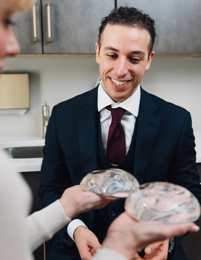 Doctor and patient sitting in a examination room and looking at two breast implants in the patients hands. - Breast augmentation in Wayne, PA