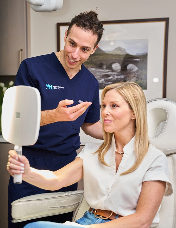 Medical professional explaining facial analysis results to female patient using mirror in consultation room - Dermal fillers in Wayne, PA