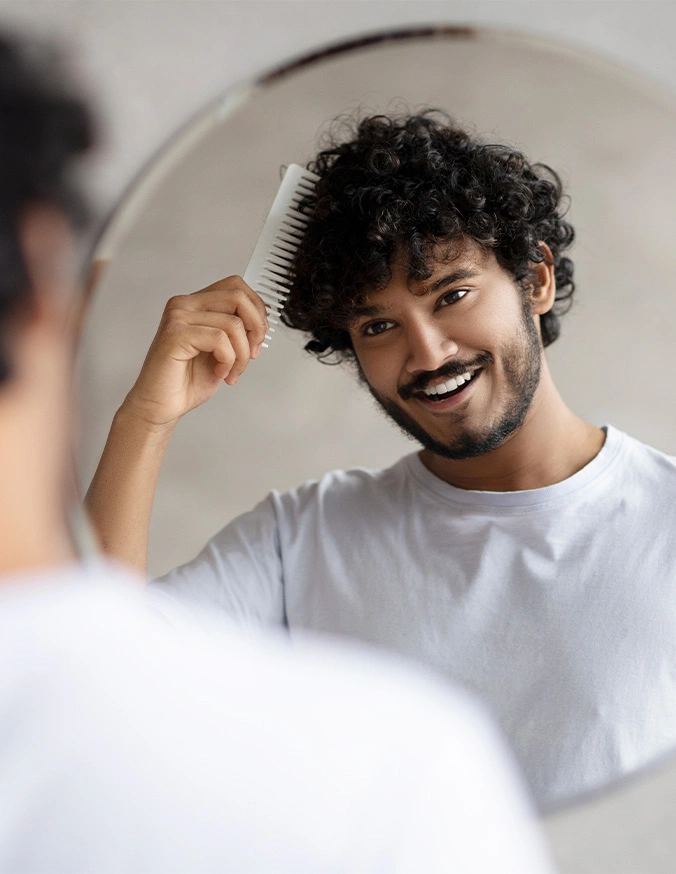 Man with curly hair smiling while brushing hair in front of bathroom mirror - Finasteride and mindoxidle in Wayne, PA