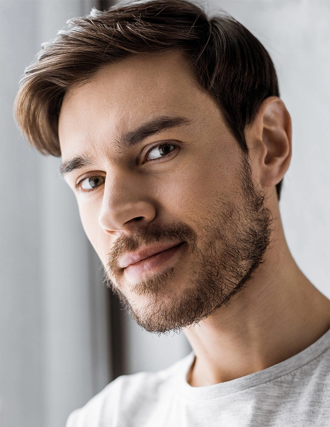Smiling man with beard and styled hair wearing white t-shirt against light background - Otoplasty in Wayne, PA
