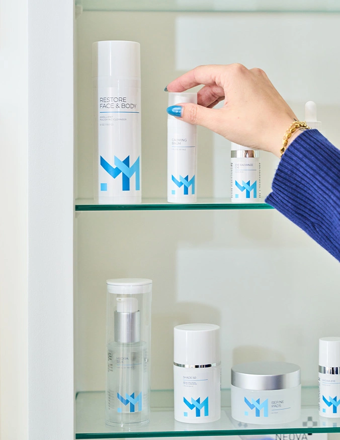 Hand reaching for skincare product with blue butterfly logo on glass shelf in bathroom cabinet - Skincare line in Wayne, PA