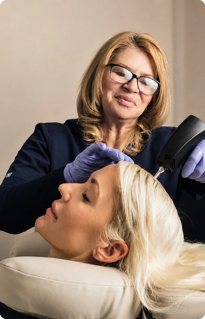 Professional administering cosmetic injection treatment to patient lying down in medical office setting - Hair in Wayne, PA