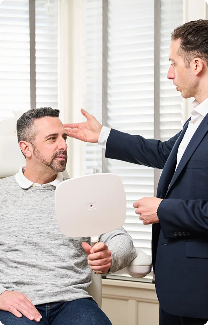 Doctor Marc Govert and patient having a discussion in an office, one seated and one standing holding a mirror - Hair in Wayne, PA