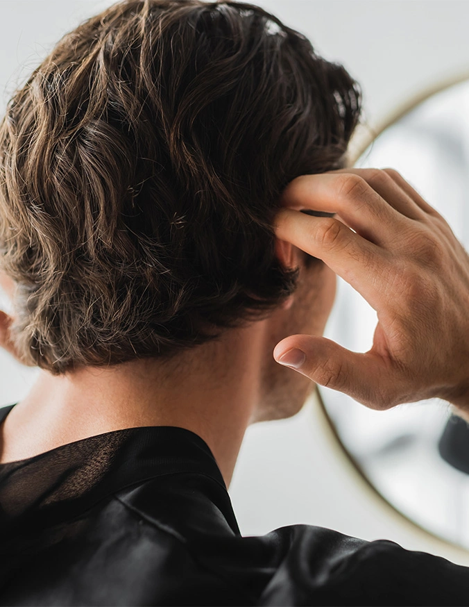 Person scratching their head with hand, viewed from behind showing dark wavy hair and black clothing - Nutrafol in Wayne, PA