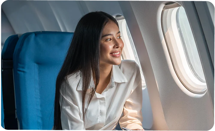 Woman in white shirt smiling while looking out airplane window during flight - in Wayne, PA