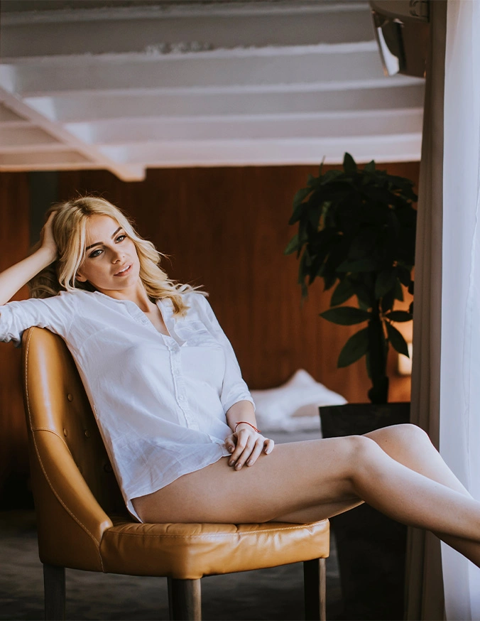 Woman relaxing in white outfit on tan leather chair in modern interior space - Thigh lift in Wayne, PA